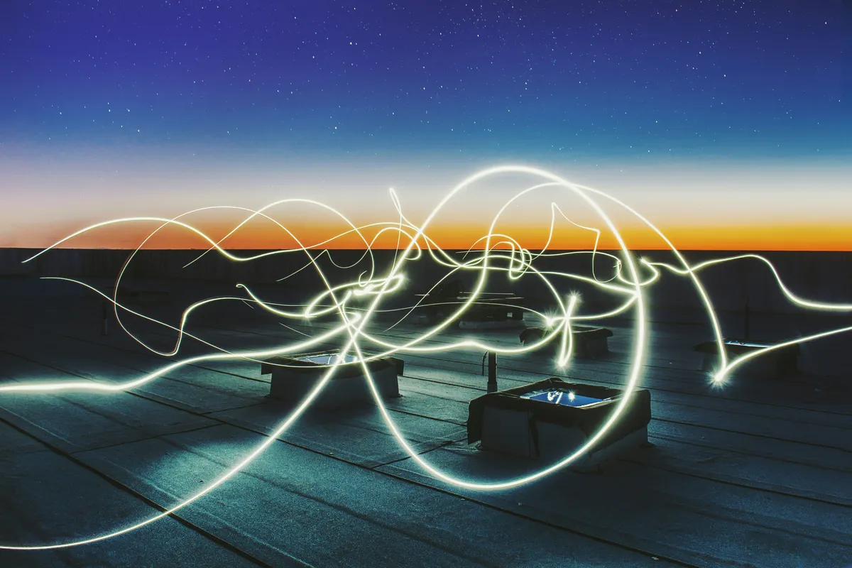 Tangled light trails over a rooftop at dusk.