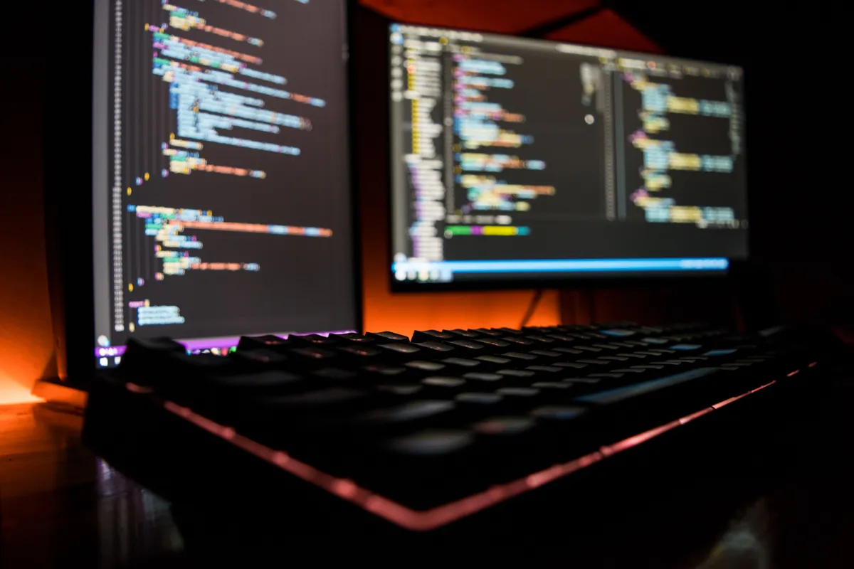 Backlit keyboard in front of two monitors showing code.
