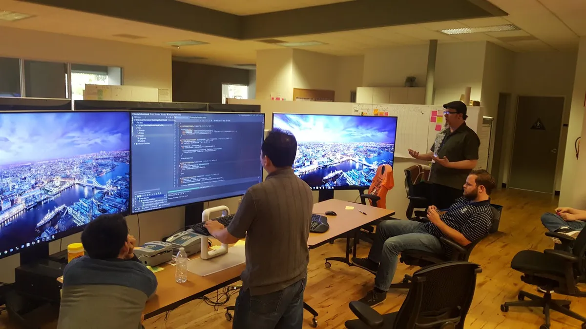 A team programming together in front of large screens in an office; one person types while the others watch and discuss.